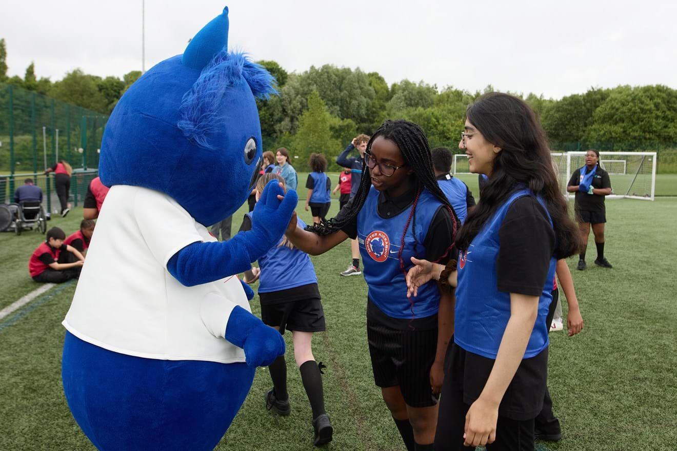 Two girls giving a high five to a blue monster mascot